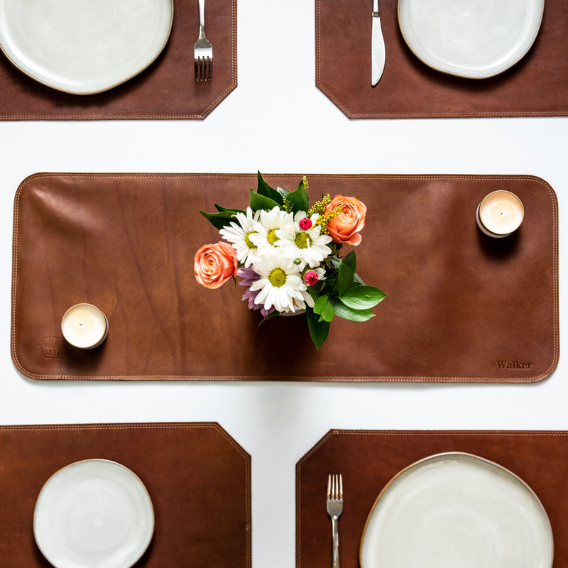 Table set with a fine leather table runner, flower, candles, and fine leather placemats